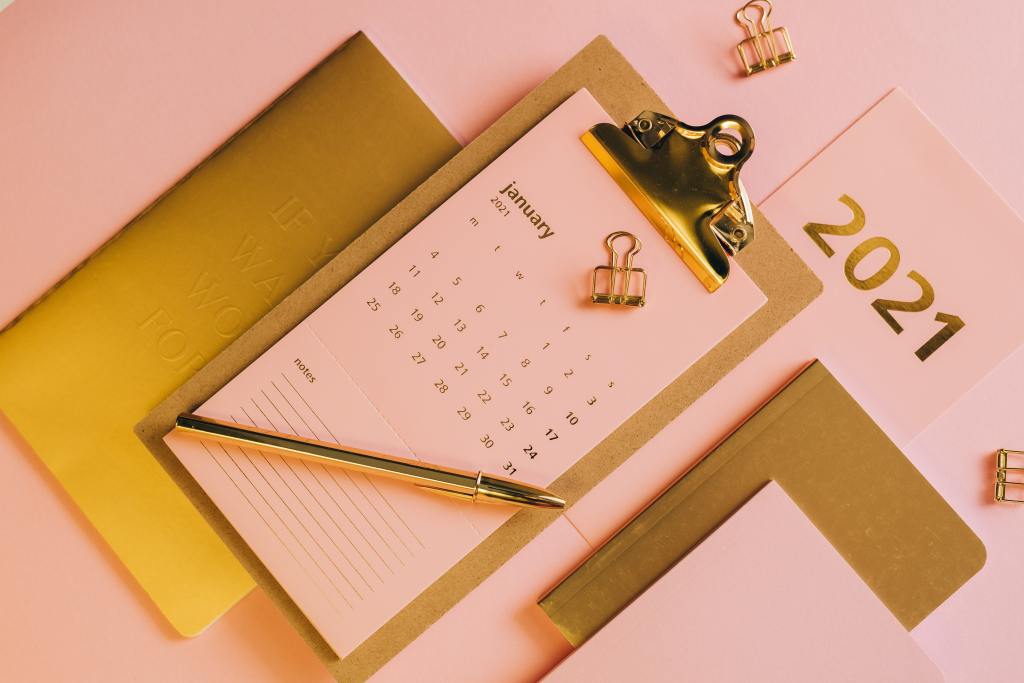 Gold embossed notebook, light pink calendar with gold writing on clipboard with gold clip.